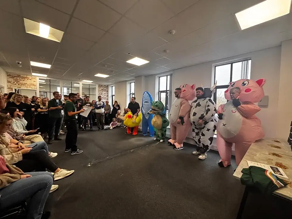 People in animal costumes, including a duck, pig, and cow, stand in a crowded room with onlookers. RiskSTOP Group's office Olympics in full flow.
