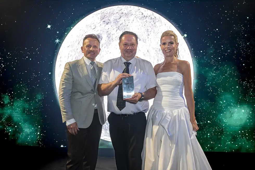 Danny Lillington poses with a trophy, alongside Spotlight Award hosts, in front of a giant moon and starry sky backdrop.