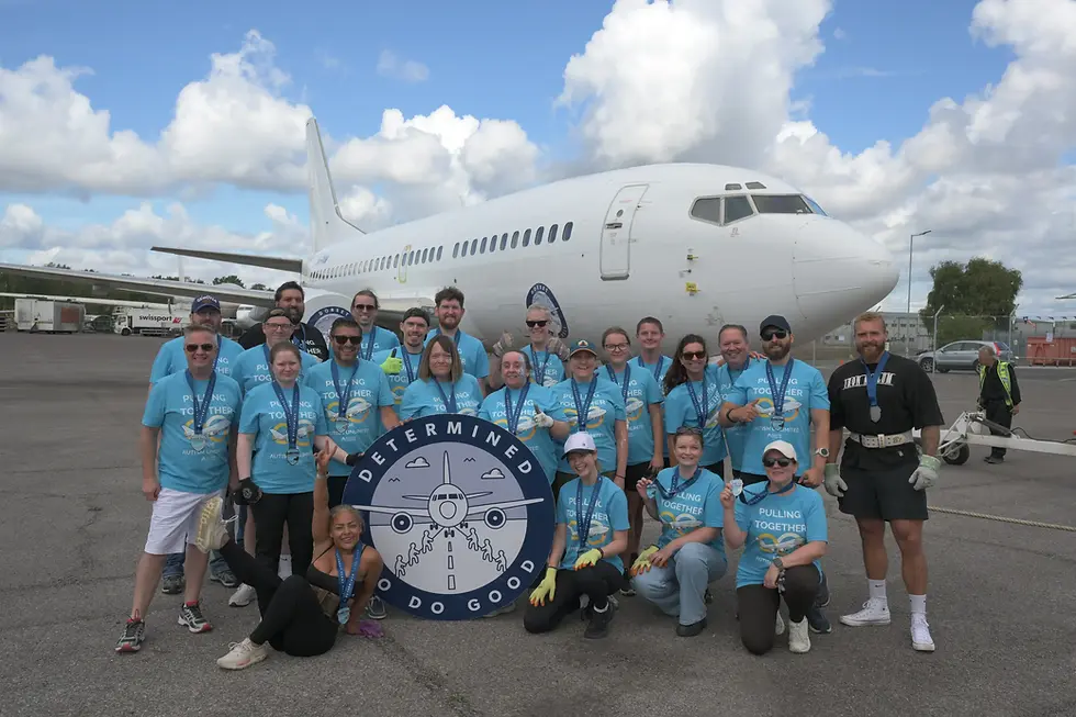 Flight Risk team posing on airport tarmac in front of a white Boeing 737, holding a DETERMINED TO DO GOOD sign.