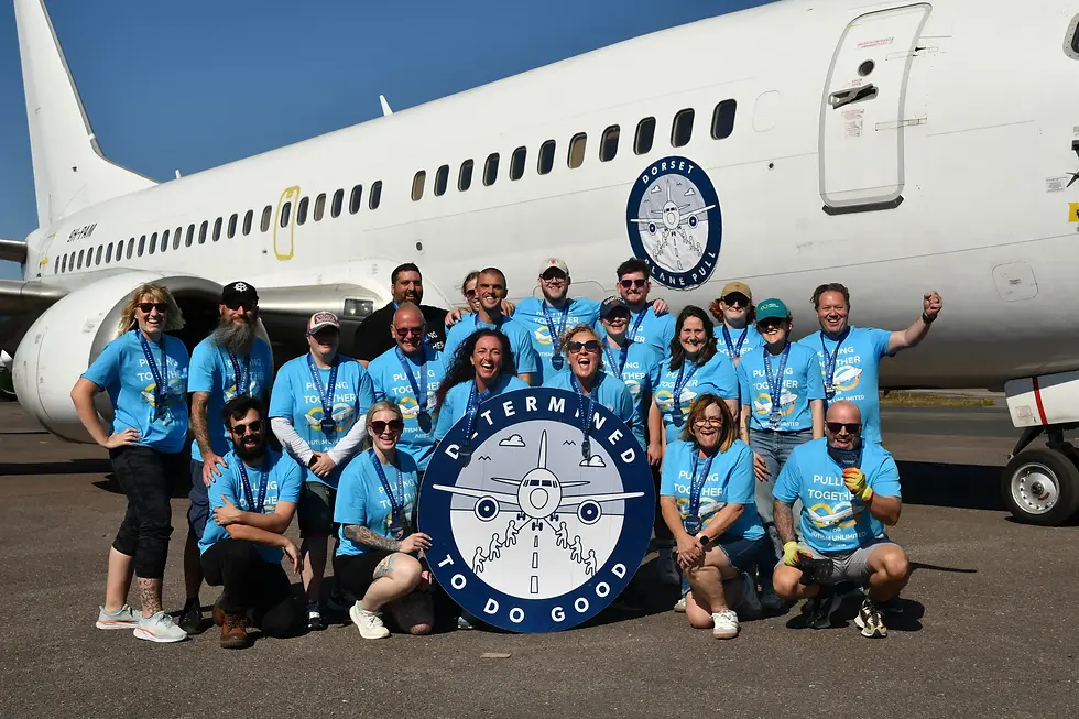 RiskSTOP Group team in blue shirts pose happily in front of a plane, holding a sign reading "Determined to Do Good."